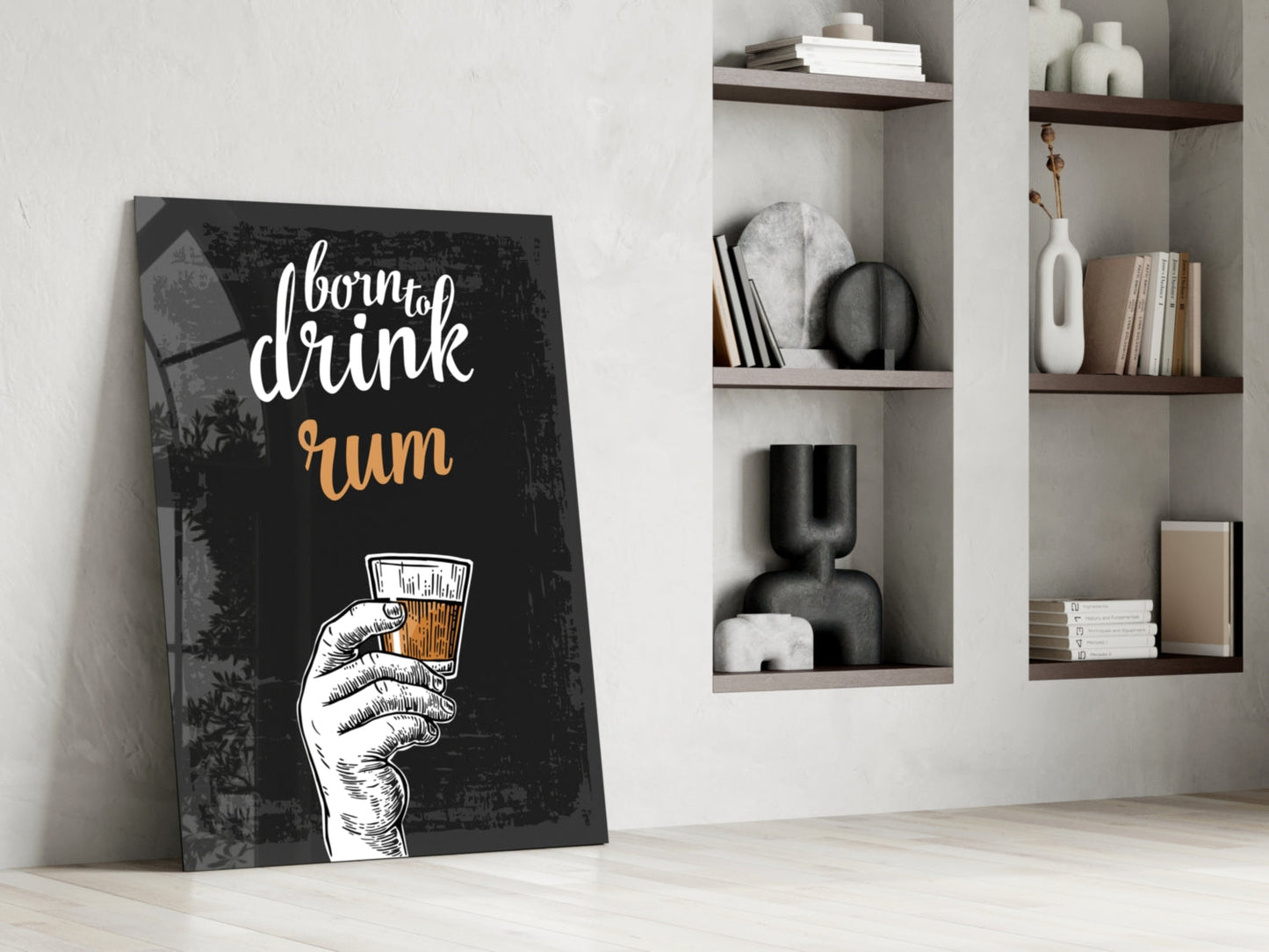 Black canvas rum wall art leaning against white wall beside floating shelves with decorative objects and books.