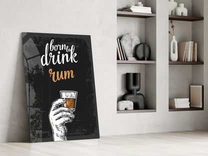 Black canvas rum wall art leaning against white wall beside floating shelves with decorative objects and books.