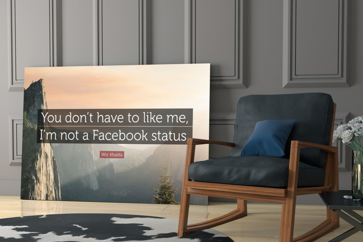 Glass wall art displaying a misty mountain valley landscape with white text reading "You don't have to like me, I'm not a Facebook status" attributed to Wiz Khalifa, displayed in a modern interior setting next to a wooden chair.
