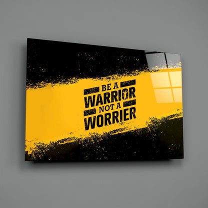 Glass wall art with yellow and black grunge design displaying "BE A WARRIOR NOT A WORRIER" text, angled view against gray background.
