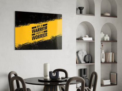 Yellow and black motivational glass wall art reading "BE A WARRIOR NOT A WORRIER" displayed above a dining table in a modern interior.
