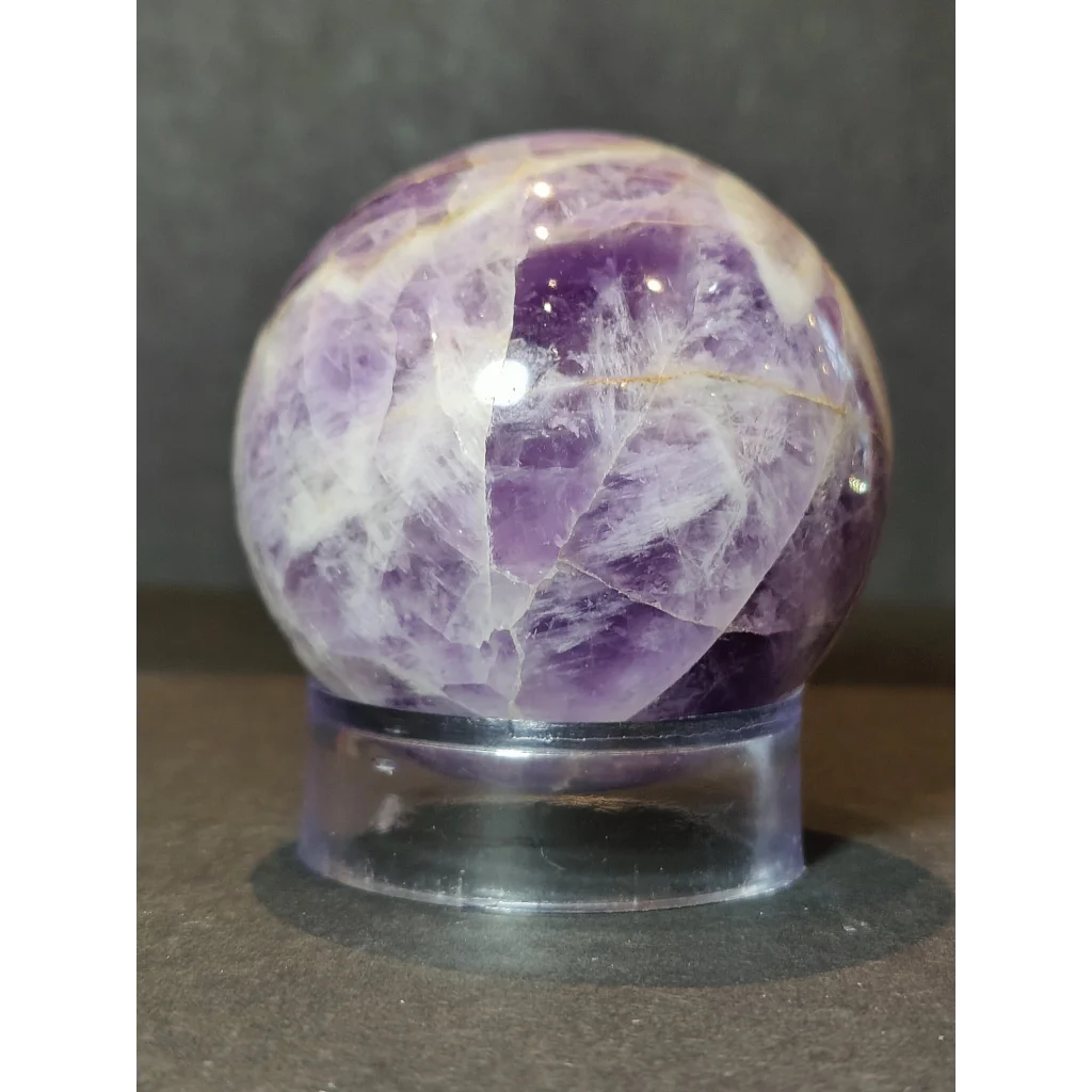 Chevron amethyst polished sphere sculpture featuring a purple and white amethyst polished sphere with natural crystals on an acrylic stand