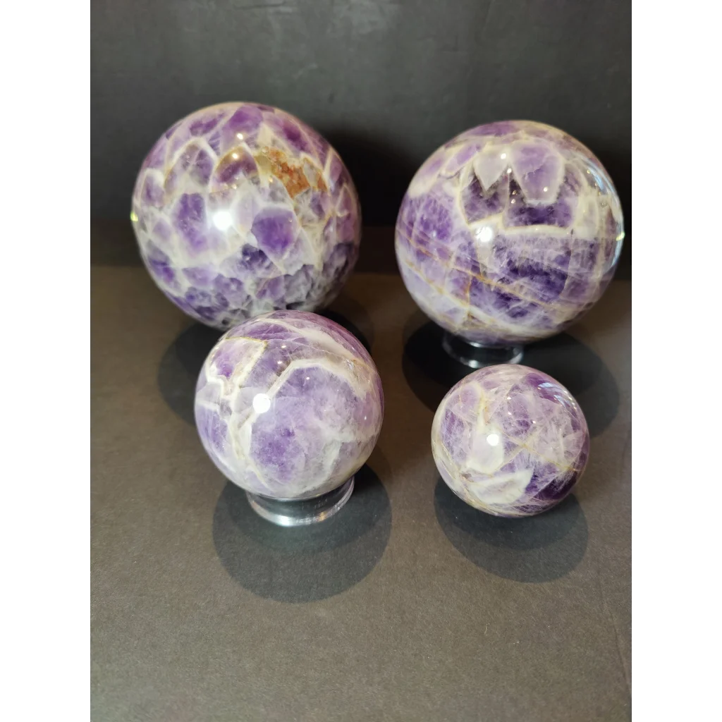 Four chevron amethyst polished spheres displaying vibrant purple hues with white and golden veining patterns in sculpture form