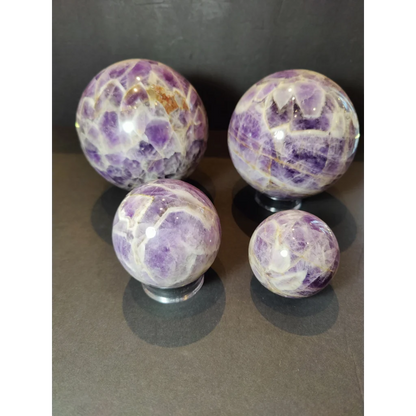 Four chevron amethyst polished spheres displaying vibrant purple hues with white and golden veining patterns in sculpture form