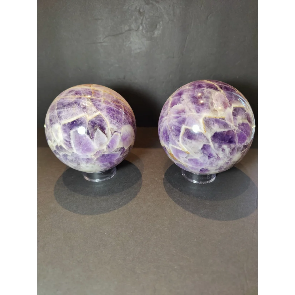 Two chevron amethyst polished sphere sculptures with vibrant purple crystals and white golden veins on clear stands