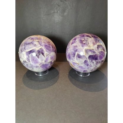 Two chevron amethyst polished sphere sculptures with vibrant purple crystals and white golden veins on clear stands