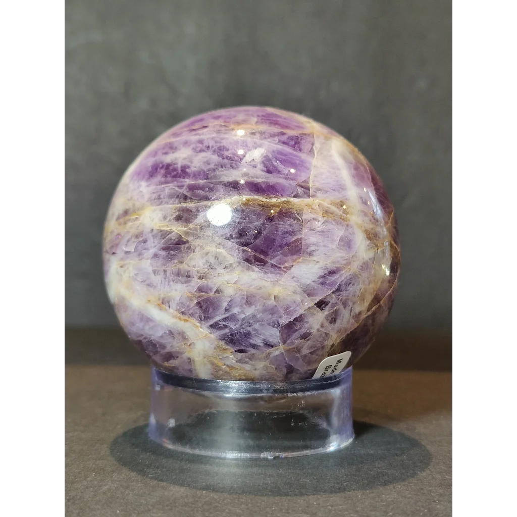 Chevron amethyst polished sphere sculpture featuring intricate white and golden crystalline patterns on a clear stand
