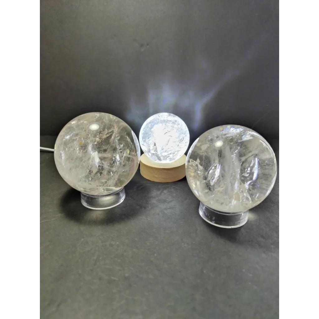 Three clear quartz polished spheres on transparent bases with center sphere illuminated as polished sphere sculpture