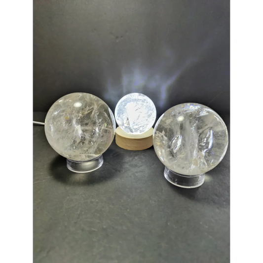 Three clear quartz polished spheres on transparent bases with center sphere illuminated as polished sphere sculpture