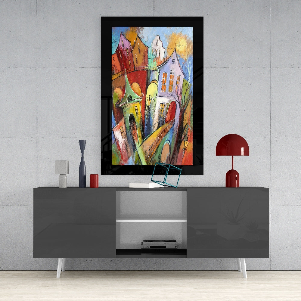Colorful framed glass wall art depicting whimsical multicolored houses displayed above gray media console in modern interior setting.