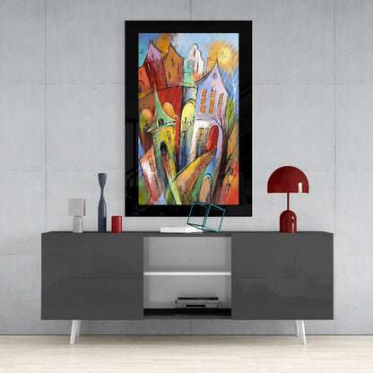 Colorful framed glass wall art depicting whimsical multicolored houses displayed above gray media console in modern interior setting.