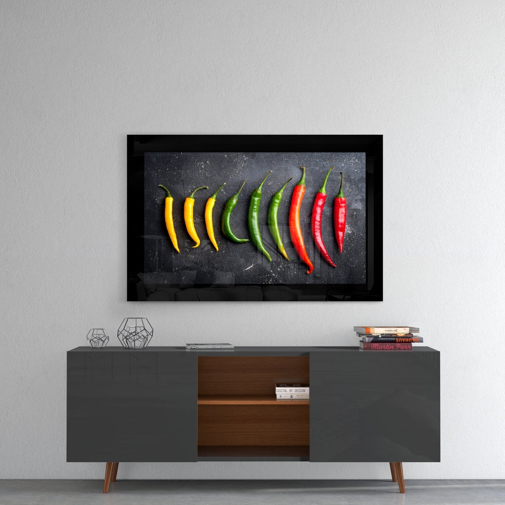Framed glass wall art displaying a gradient arrangement of yellow, green, and red chili peppers on dark background, mounted above mid-century modern credenza.
