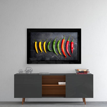 Framed glass wall art displaying a gradient arrangement of yellow, green, and red chili peppers on dark background, mounted above mid-century modern credenza.
