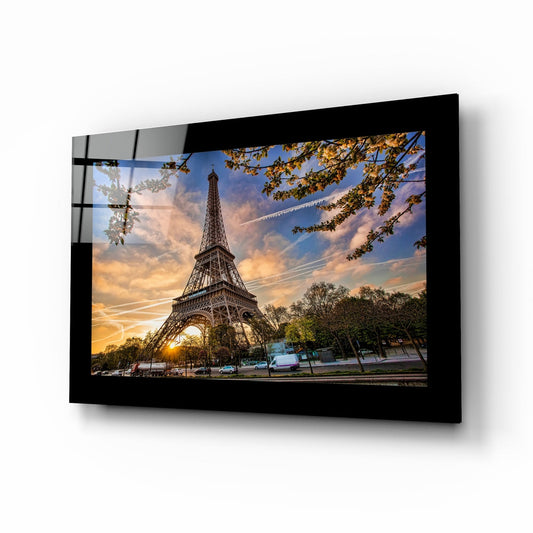 Black-framed glass wall art displaying the Eiffel Tower at sunset with golden sky, autumn foliage, and Parisian street scene, mounted at an angle.