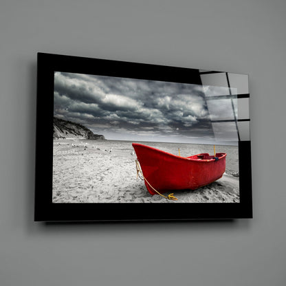 Red fishing boat beached on gray sand with stormy sky, displayed in black framed glass wall art mounted on gray wall.