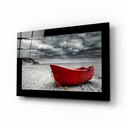 Black-framed glass wall art displaying a red fishing boat on a beach with stormy sky, mounted on white wall.