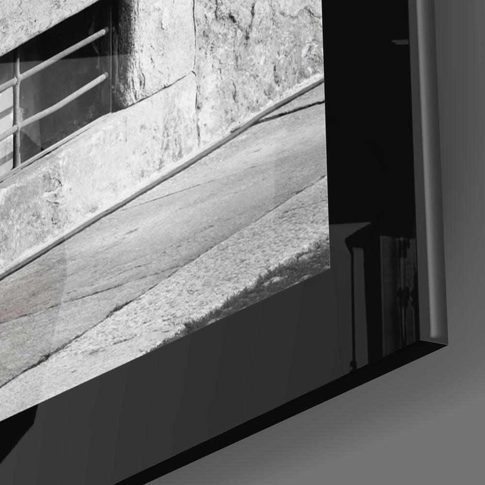 Close-up of black framed glass wall art edge showing weathered wooden planks and metal railing in black and white.