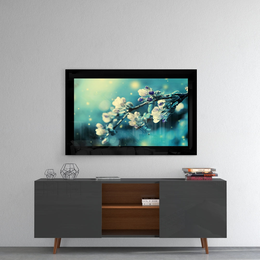Framed glass wall art displaying delicate white blossoms on turquoise background, mounted above dark wood media console.