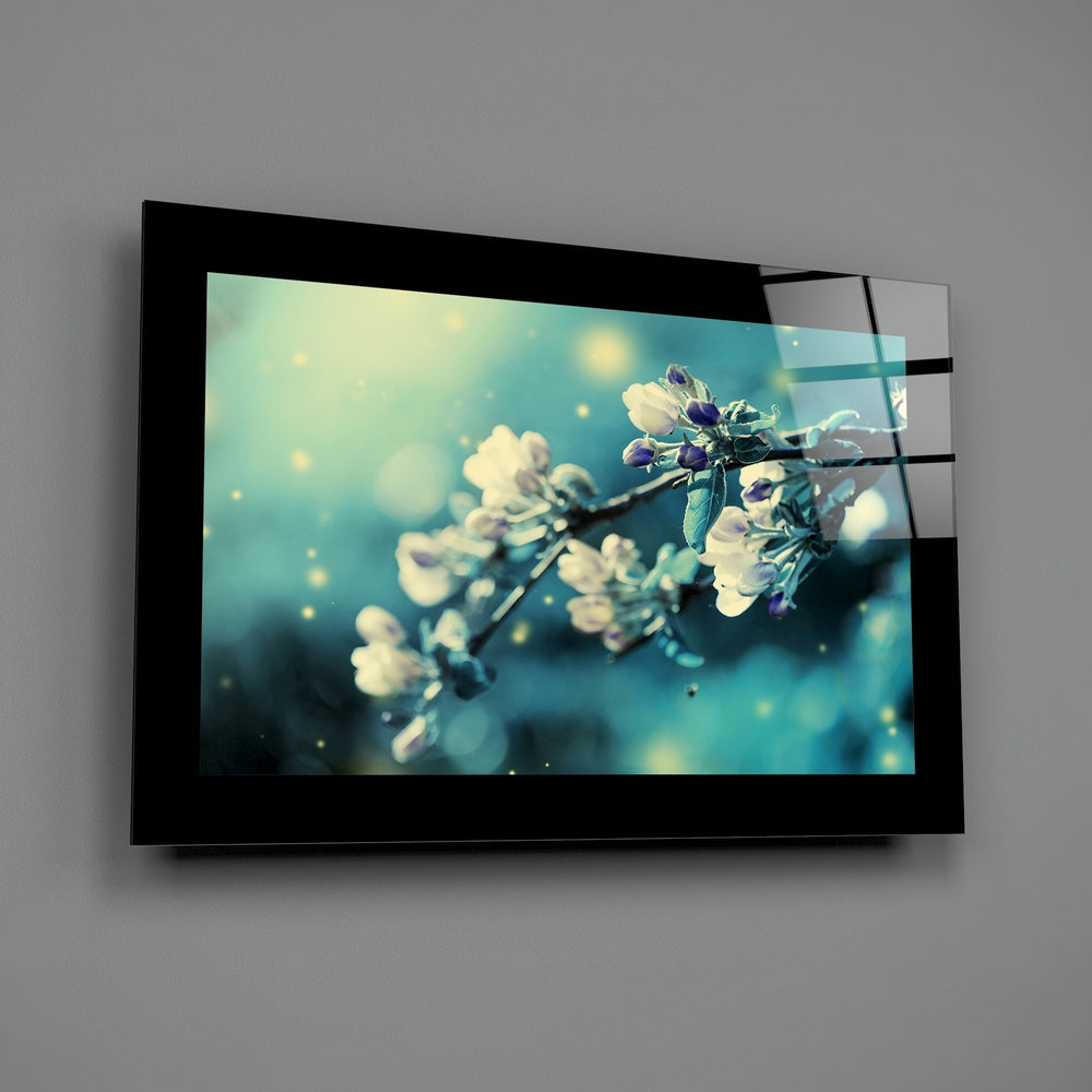 Black-framed glass wall art displaying close-up photograph of delicate white and purple flowers on turquoise background, mounted on gray wall.