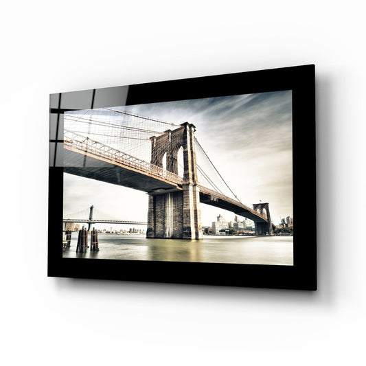 Black-framed glass wall art displaying Brooklyn Bridge photograph mounted on white wall, angled perspective view.