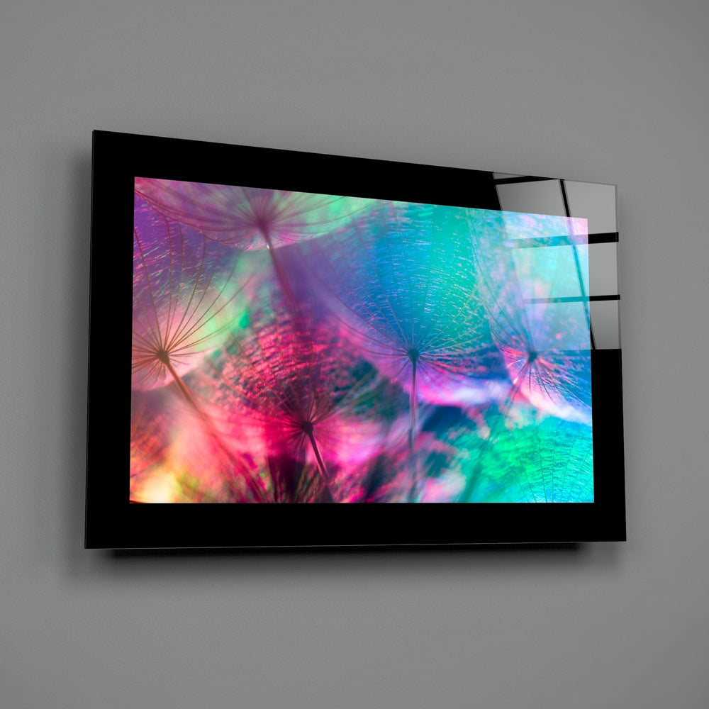 Black-framed glass wall art mounted on gray wall displaying vibrant rainbow-colored dandelion flowers in pink, purple, blue, and green hues.