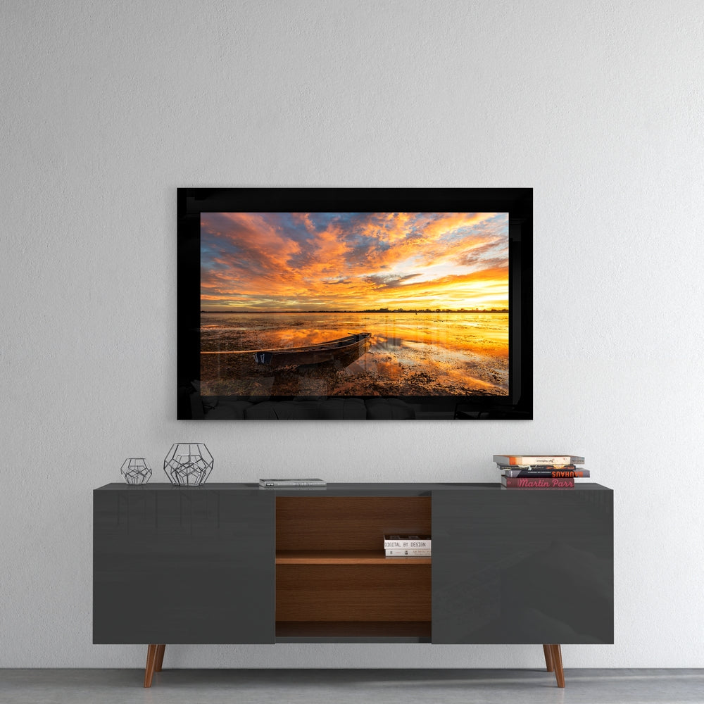 Framed glass wall art displaying a sunset beach scene with boat, mounted above a mid-century modern credenza in a living room setting.