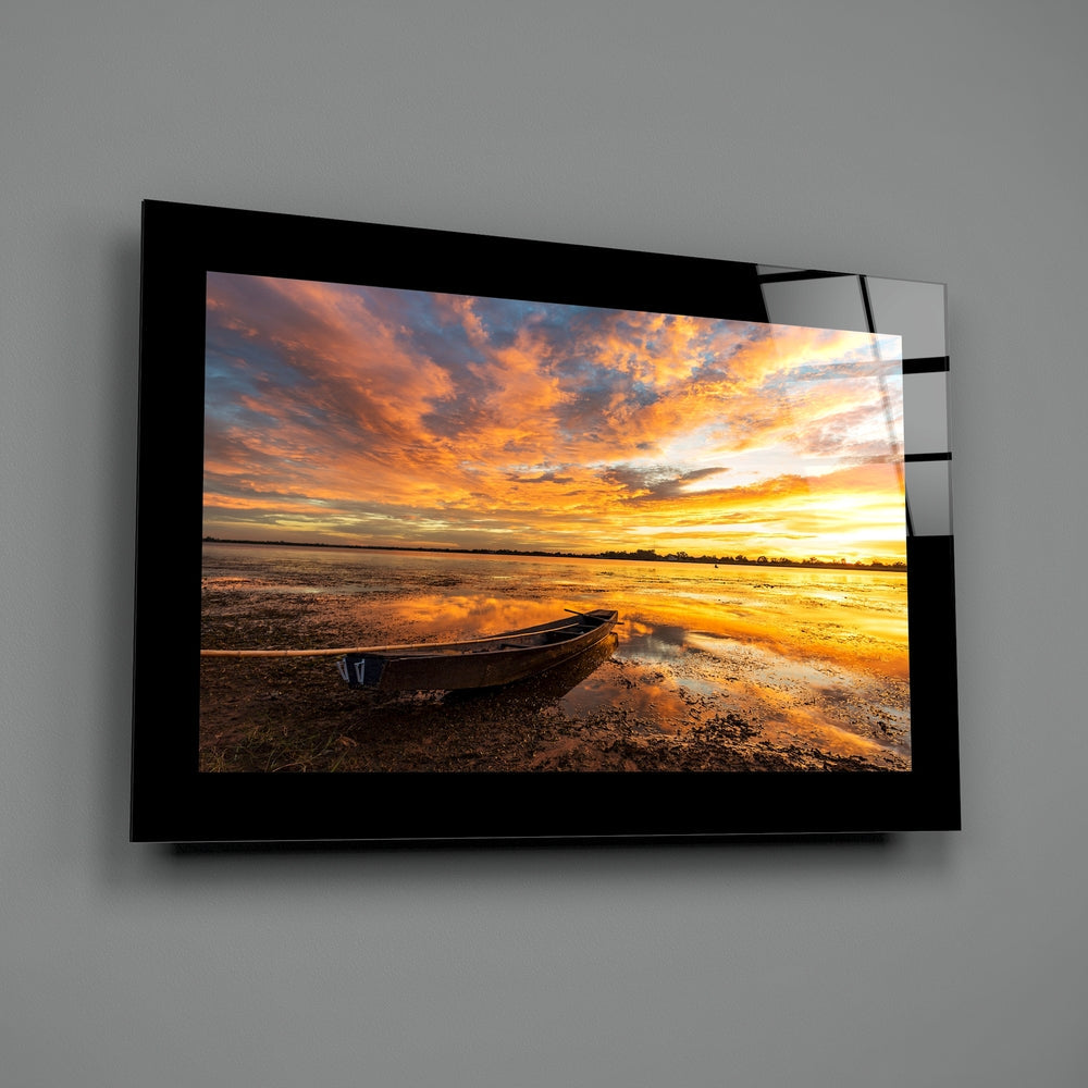 Wall-mounted glass art panel displaying a sunset beach scene with boat, golden sky, and reflective water against gray wall.