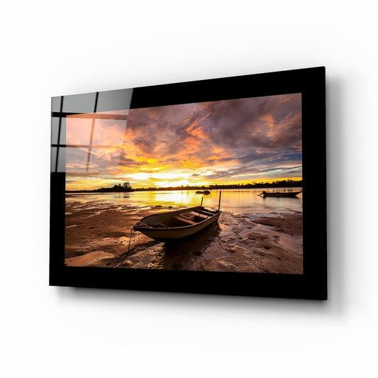 Black-framed glass wall art displaying a sunset landscape with a beached boat, displayed at an angled perspective against white background.