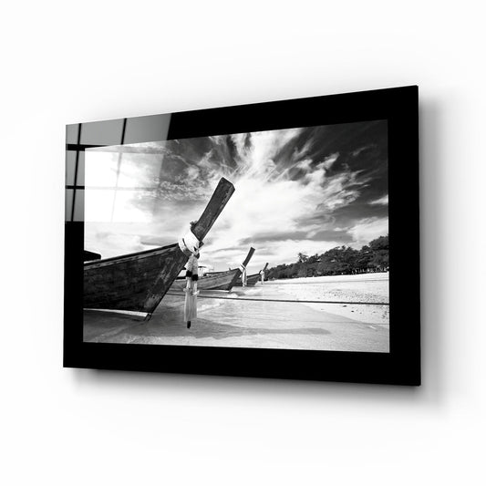 Black and white framed glass wall art displaying longtail boats anchored on a beach with dramatic cloudy sky, shown at an angled perspective against white background.