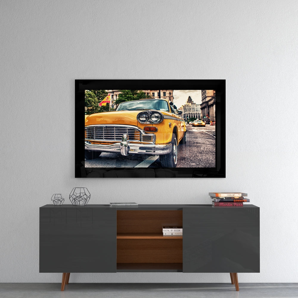 Black-framed glass wall art displaying a yellow vintage taxi cab on a city street, mounted above a mid-century modern console table.