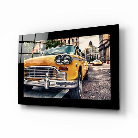 Black-framed glass wall art displaying a bright yellow vintage taxi cab on an urban street with classic buildings in the background.