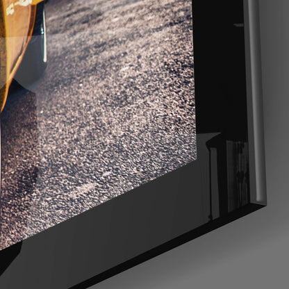 Close-up angled view of framed glass wall art showing textured asphalt road surface with yellow vehicle edge visible.