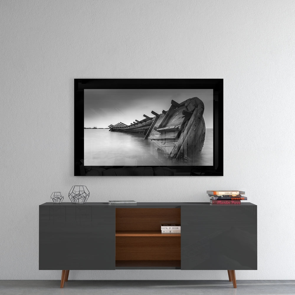 Black-framed glass wall art depicting a wrecked wooden boat in shallow water, displayed above a dark gray and wood media console.