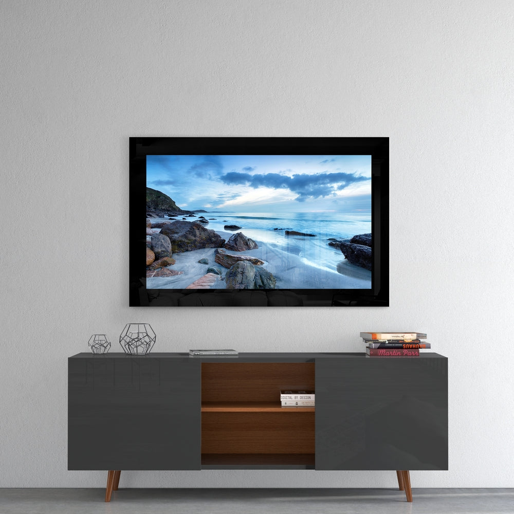 Coastal glass wall art displaying a blue ocean sunset with rocky beach mounted above a mid-century modern credenza.
