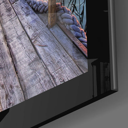 Close-up angled view of glass wall art edge showing weathered wood texture, blue-toned rope detail, and black frame mounting against gray wall.