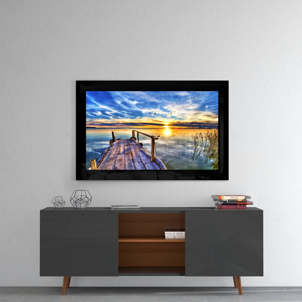 Framed sunset pier glass wall art displayed above a modern two-tone media console in a minimalist living room setting.