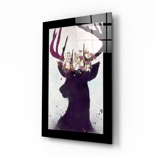 Angled perspective view of framed glass wall art featuring a dark silhouetted deer head with purple ribbon and floral crown in warm tones against white background.