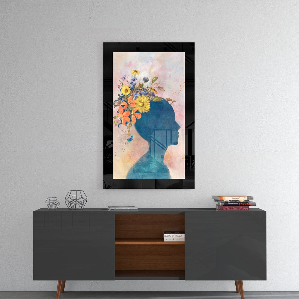 Framed glass wall art depicting a blue silhouette profile with colorful flowers blooming from the head, hung above a mid-century modern credenza.
