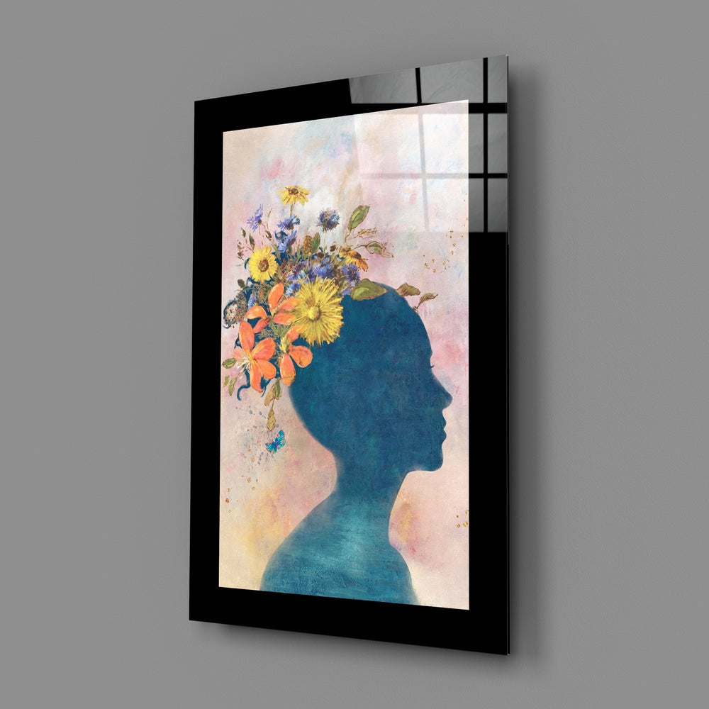 Angled view of framed glass wall art featuring a blue silhouette profile with colorful flowers emerging from the head against a soft watercolor background.