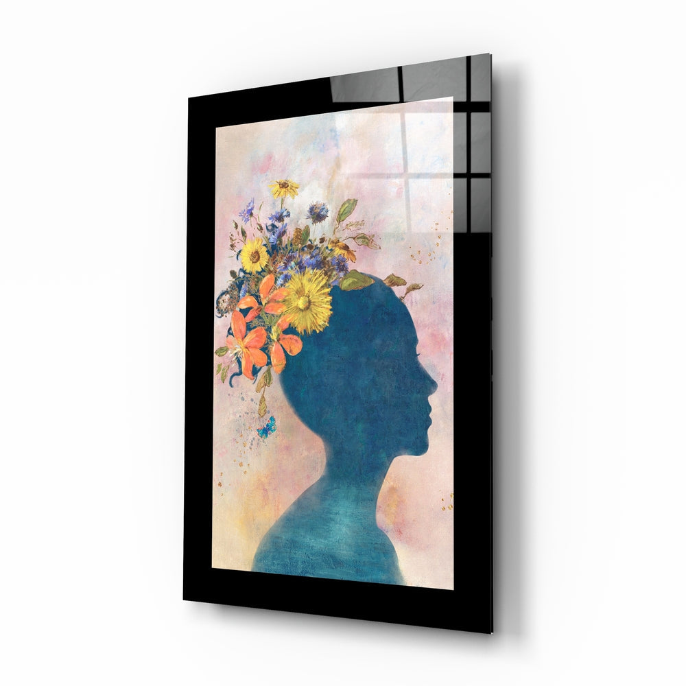 Angled view of framed glass wall art featuring a blue silhouetted profile with colorful flowers emerging from the head against a soft, pastel background.