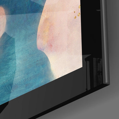 Close-up angled view of glass wall art showing blue and cream watercolor abstract design with gold accents mounted in black frame.