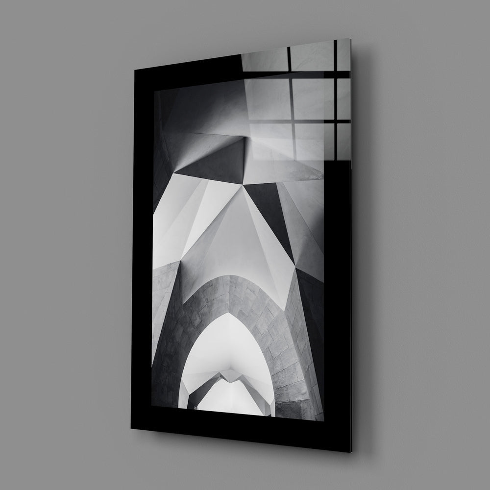 Black-framed glass wall art displaying upward architectural photography in grayscale, mounted at angle against gray background.