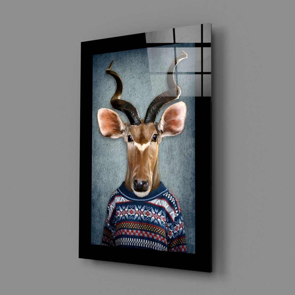 Framed glass wall art displaying an anthropomorphic kudu wearing a navy and red patterned sweater, mounted at an angle against gray wall.