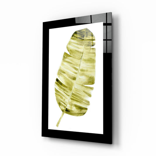 Black-framed glass wall art displaying a single watercolor palm leaf in olive and yellow-green tones, angled perspective view.