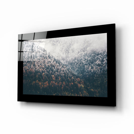 Black-framed glass wall art displaying a misty forest landscape with evergreen trees in autumn colors, mounted at an angle against a white background.