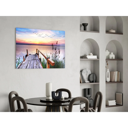 Serene sunset over water on glass wall art with dock, reeds, birds