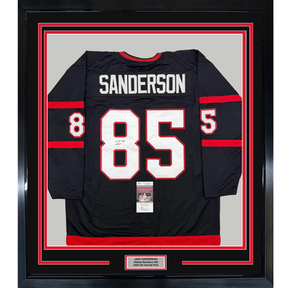 Black hockey jersey with red and white trim displaying "SANDERSON" and number "85" in white, framed with red and black matting and JSA authentication certificate visible at bottom.