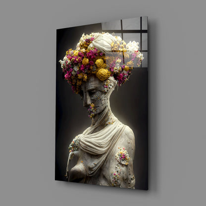 Glass wall art panel displaying a classical stone bust adorned with vibrant magenta, yellow, and white flowers against a dark background.