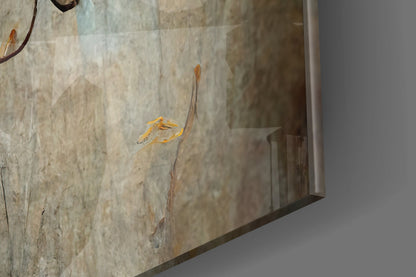 Close-up angled view of glass art panel featuring golden-yellow hand-painted flowers on stem against textured neutral background.