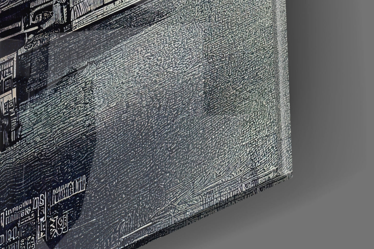 Close-up angled view of textured glass wall art showing detailed etched patterns and monochromatic grayscale surface with visible text along edges.
